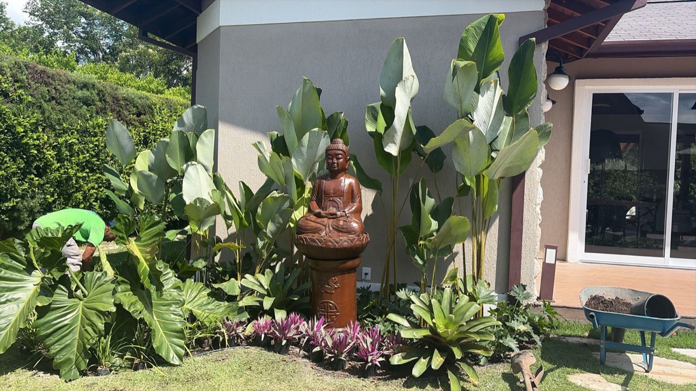 Canteiro tropical com escultura de Buda e folhagens altas junto à casa